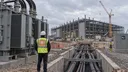 A visitor wearing an Anthropic logo patch looks across a large data-center construction site with power equipment and heavy cables.