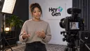 A person makes a small hand gesture in front of a camera in a HeyGen-branded video studio.
