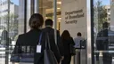Several people walk through glass doors beneath a sign reading “Department of Homeland Security,” beside an access scanner.