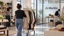 Retail workers move merchandise through a multi-brand showroom with the Marklo logo on a glass partition.