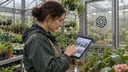 A greenhouse worker uses a tablet displaying a browser with several open tabs, with an OpenAI logo on the glass entrance behind them.