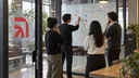 Mesmer engineers coordinate coding work around a glass workflow wall in their studio.