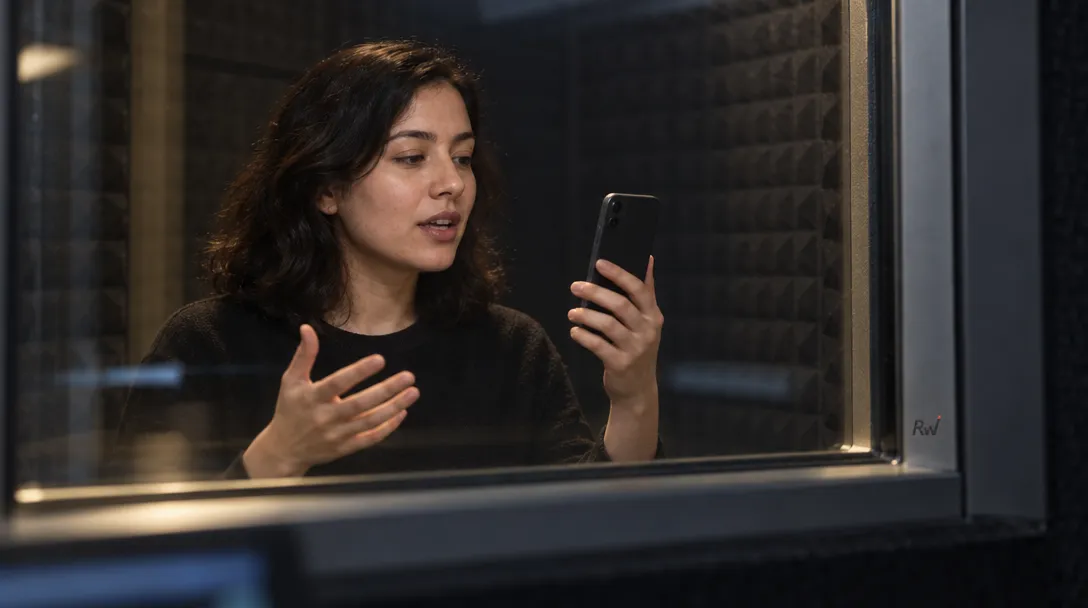 A person speaks toward a smartphone in an acoustic booth, representing Stellon Labs’ compact speech model for edge devices.