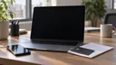 A bank card and folded financial statement sit beside a smartphone and an open laptop with a dark screen.