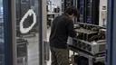 A technician inspects GPU hardware in a compute lab beside an Overshoot logo on a glass doorway.